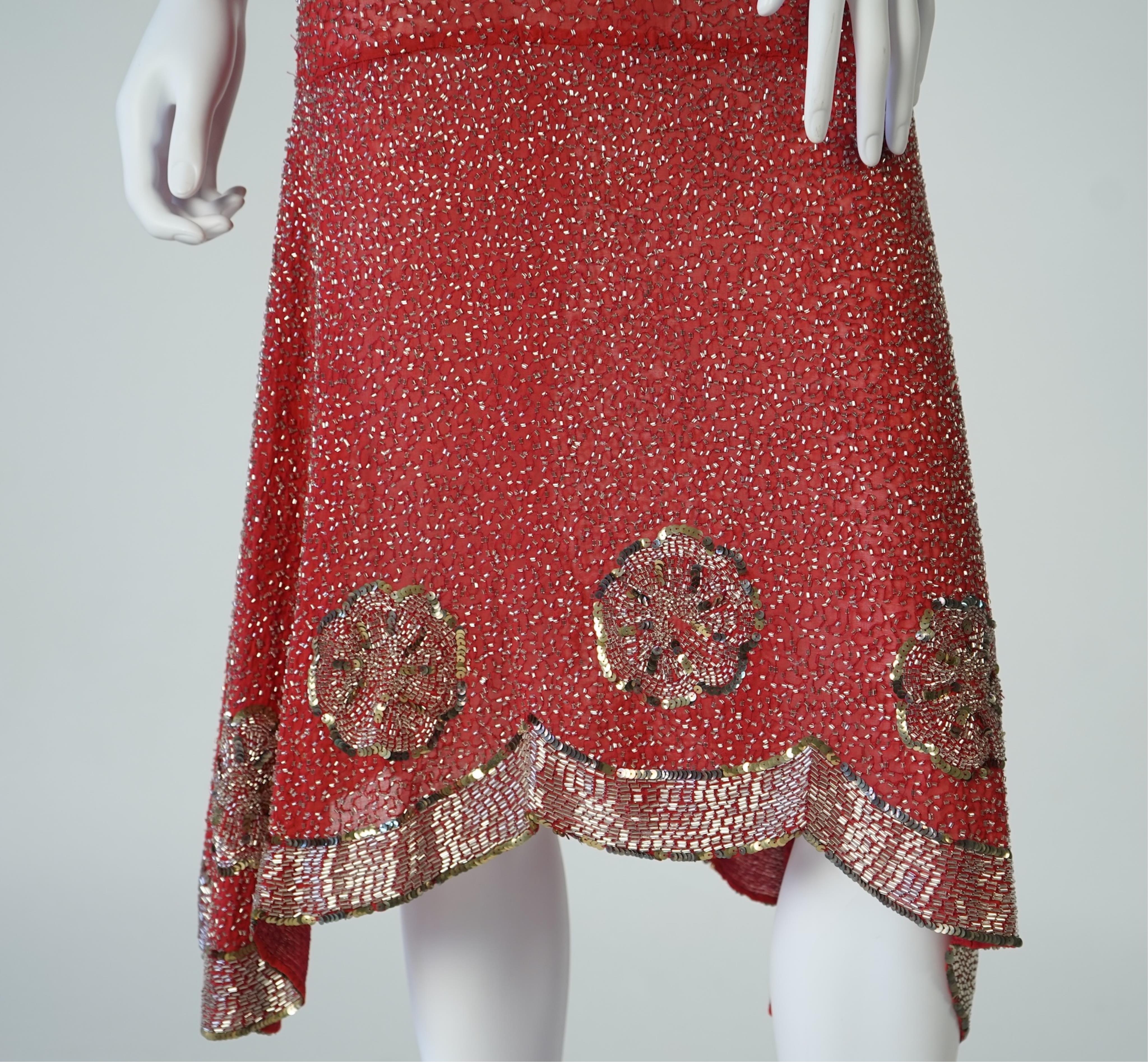 A 1920's red georgette beaded evening dress. Hand beaded and sequinned in white and gold, designed with a dropped waist, handkerchief points and wide beaded border with large stylistic floral motifs. Length 115cm. Condit